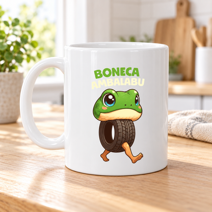 Vit mugg med texten Boneca Ambalabu och en tecknad figur med grönt grodhuvud, däck som kropp och två ben.
