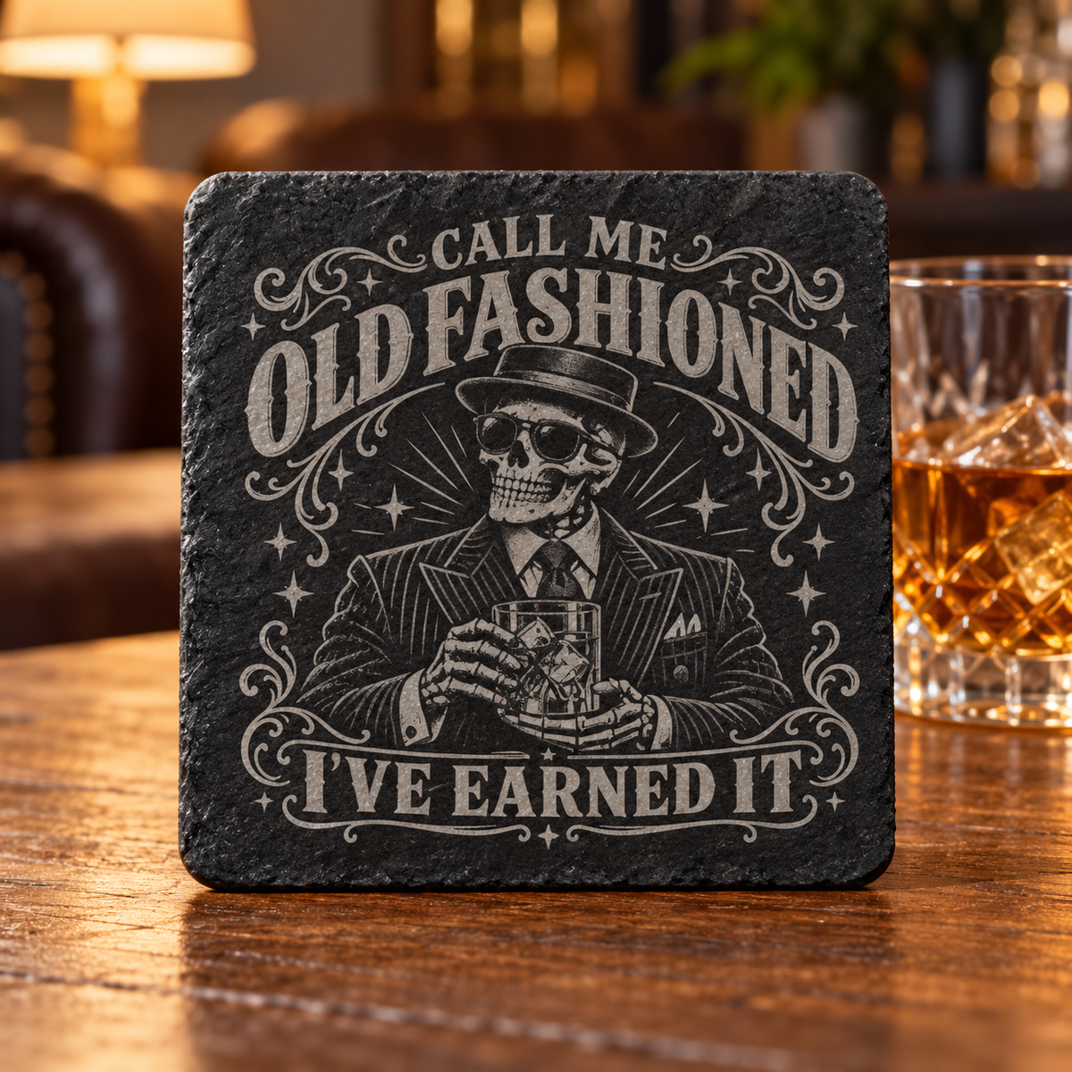 Glasunderlägg i skiffer med graverat skelett i kostym och hatt samt texten Call Me Old Fashioned – I’ve Earned It.