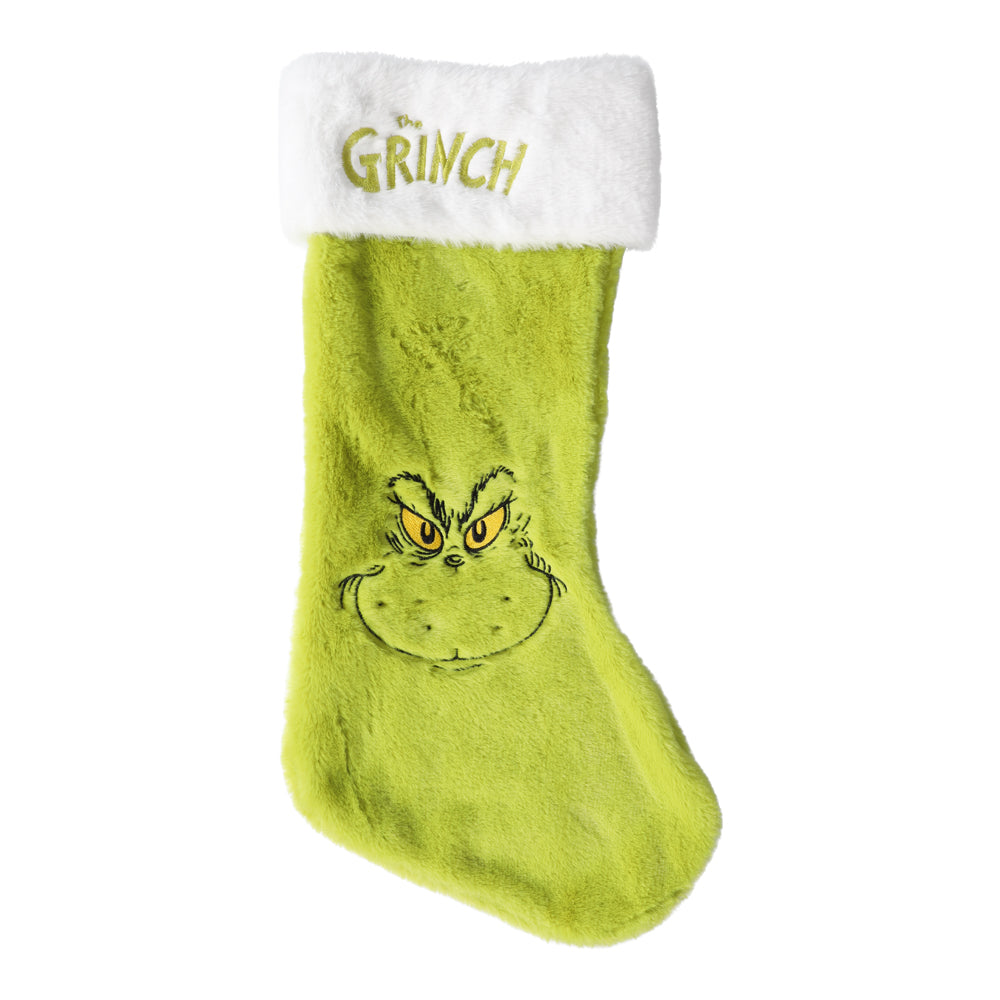 En grön och röd julstrumpa med ett busigt motiv av Grinchen hängande vid en öppen spis.