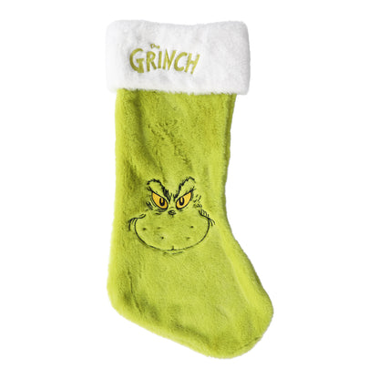 En grön och röd julstrumpa med ett busigt motiv av Grinchen hängande vid en öppen spis.