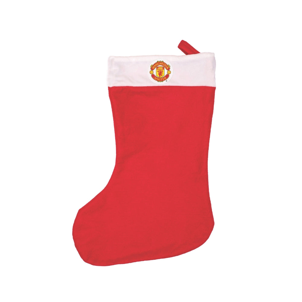 En klassisk röd julstrumpa prydd med Manchester Uniteds klubbmärke hängande vid en eldstad.